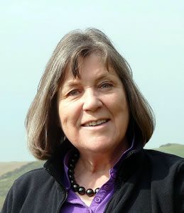 Rhian Samuel - photographer unknown Welsh composer Rhian Samuel stands outside with a hill in the distance. She has shoulder length hair & wears a purple top with black jacket