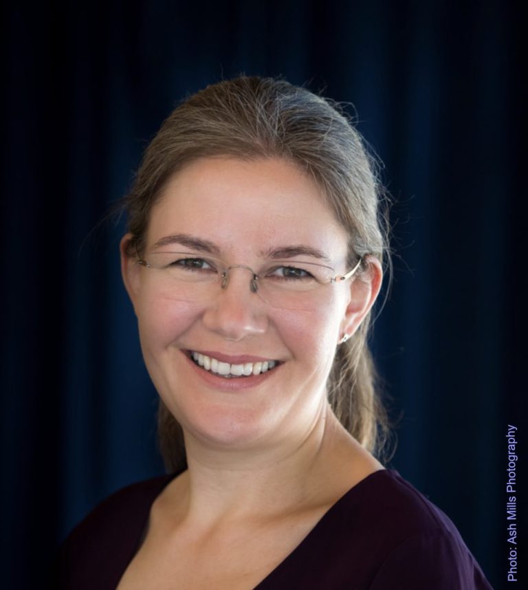 Olivia Sparkhall ©Ash Mills Photography headshot of composer Oliiv Sparkhall. She faces the camera and wearing a purple top and rimless spectacles