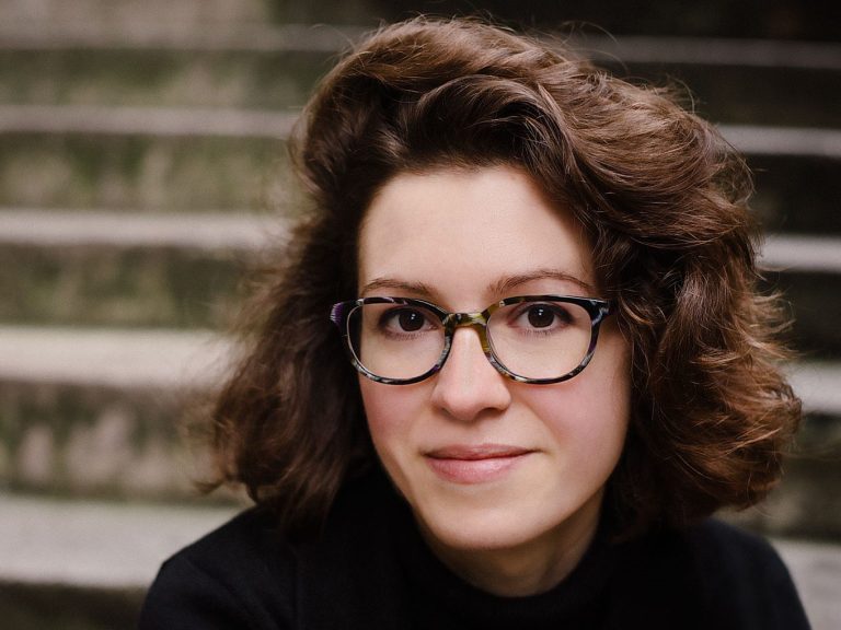 composer Libby Croad with thick wavy brown hair and wide rimmed glasses, wearing a black concert jacket