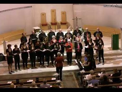 Italian composer Angelina Figus wearing black trousers and a  red jacket conducting a choir of girls and women in a church 