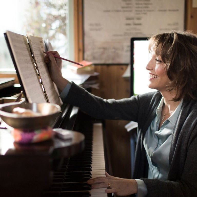 Roxanna Panufnik ©Benjamin Ealovega Photography composer Roxanna Panufnik sits at her grand piano making edits with a pencil to a composition which sits on the piano music stand