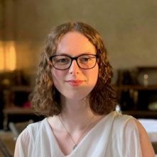 Helen Paish - photographer unknown young composer Helena Paish, with shoulder length curly hair, wide rimmed glasses, wearing a white top and fine necklace