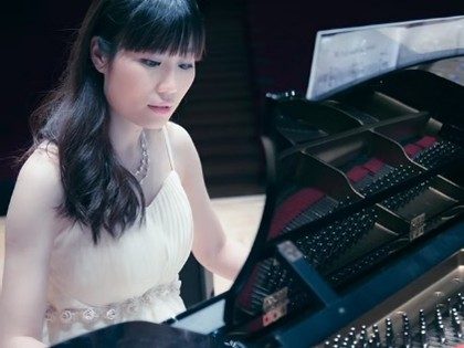 Kiko Shao - photographer unknown composer Kiko Shao plays a grant piano. She is wearing a white evening dress and wearing a silver coloured necklace