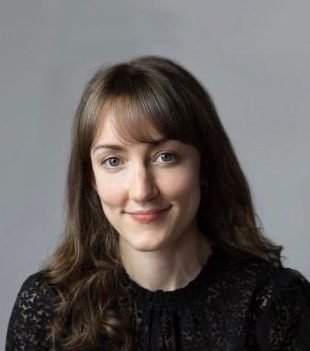 Kerensa Briggs - photographer unknown composer Kerensa Briggs, with long wavy brown hair, wearing a smart black lace blouse and smiling at the camera